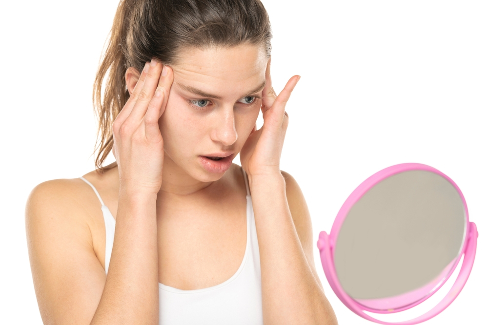 Concerned woman checking her face in the mirror for potential side effects after Dysport treatment.