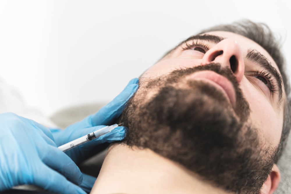 Man undergoing Botox treatment for TMJ relief, close-up view of injection near jawline by healthcare professional in sterile environment
